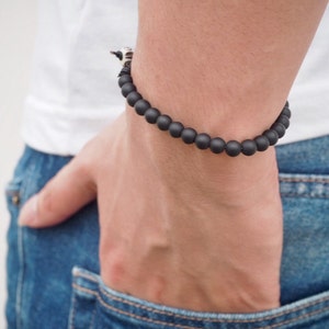 May include: A black beaded bracelet with a silver accent on a person's wrist.