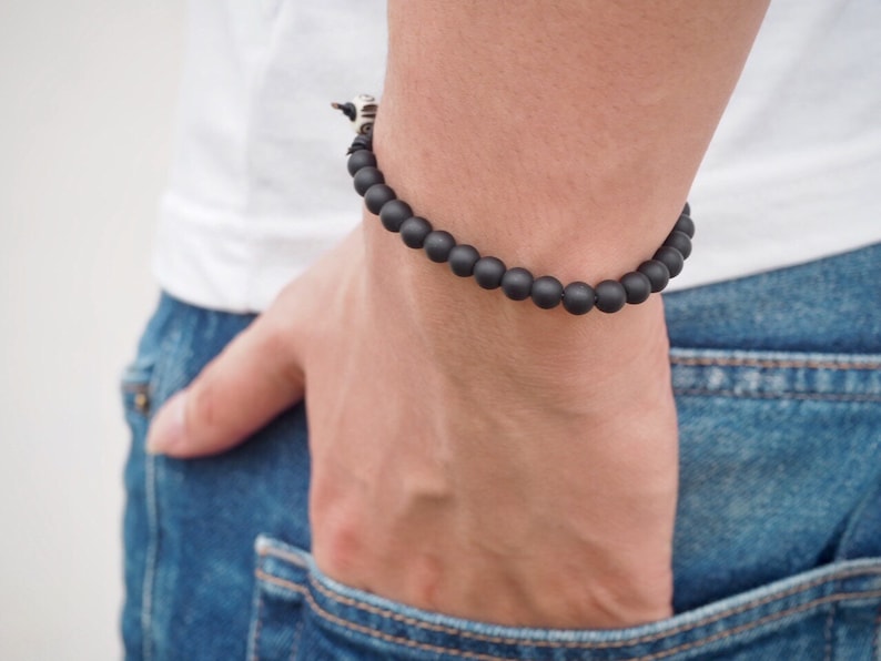 May include: A black beaded bracelet with a silver accent on a person's wrist.