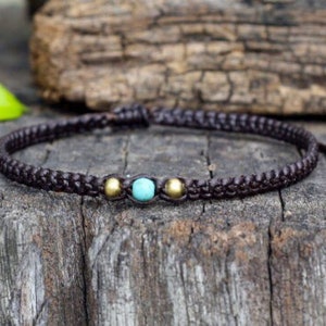 Peut inclure: Un bracelet tressé marron avec une perle turquoise et deux perles dorées.