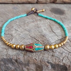 May include: A turquoise and gold beaded anklet with a red and turquoise patterned bead in the center.