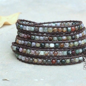 以下が含まれることがあります： 茶色の革巻きでできた、マルチカラーの宝石のブレスレット。ブレスレットは、緑、茶色、白、赤の色合いの小さな丸いビーズで作られています。革巻きは濃い茶色で、ビーズの周りを数回巻かれています。このブレスレットは、女性に人気のジュエリースタイルです。