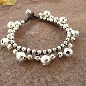 May include: A silver charm bracelet with small bells and beads on a brown cord.