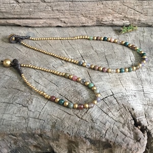 May include: Two gold beaded necklaces with colorful gemstone beads. The necklaces are on a wooden surface.