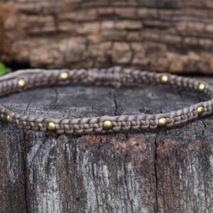 Puede incluir: Un sencillo brazalete de cordón marrón con pequeñas cuentas doradas.