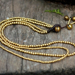 Op de afbeelding: Een gouden kralenketting met meerdere strengen en kleine belletjes aan het einde. De ketting is gemaakt van kleine, ronde kralen en heeft een eenvoudig, elegant ontwerp.