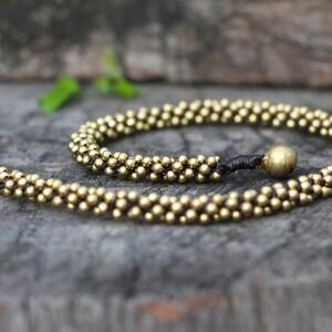May include: A gold beaded necklace with a dark brown cord and a gold bead accent. The necklace is made of small, round beads and is approximately 18 inches long.