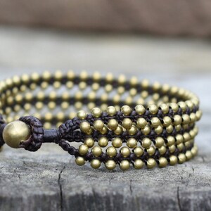 May include: A brown leather bracelet with multiple rows of gold-toned beads. The bracelet has a simple clasp closure.