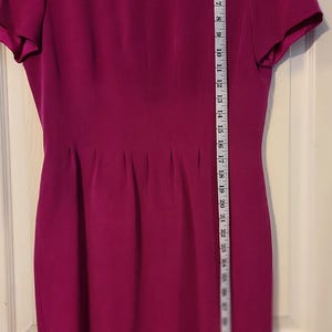 Peut inclure: Une robe magenta &agrave; manches courtes avec un col rond et une silhouette ajust&eacute;e. La robe mesure environ 94 cm de long.