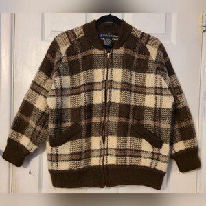 May include: A brown, cream, and tan plaid zip-up jacket with a ribbed collar, cuffs, and hem. The jacket has two front pockets and a gold zipper. The label reads "IB DIFFUSION".