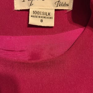 Peut inclure: Une &eacute;tiquette blanche avec du texte noir qui indique "Papell Too Petites" et "100% Soie Fabriqu&eacute; &agrave; Hong Kong 8". L'&eacute;tiquette est attach&eacute;e &agrave; un tissu de soie fuchsia.