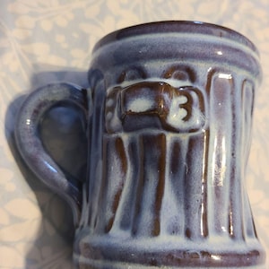 May include: A handcrafted ceramic mug with a blue and brown glaze. The mug features vertical ridges and a handle. The number "3" is visible on the front. This unique mug is perfect for coffee or tea.