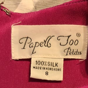 Peut inclure: Une robe en soie rose avec une &eacute;tiquette blanche qui indique "Papell's Too Petites" et "100% Soie Fabriqu&eacute; &agrave; Hong Kong" avec une &eacute;tiquette de taille 8.
