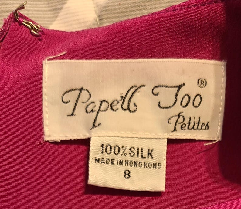 Peut inclure: Une robe en soie rose avec une &eacute;tiquette blanche qui indique "Papell's Too Petites" et "100% Soie Fabriqu&eacute; &agrave; Hong Kong" avec une &eacute;tiquette de taille 8.
