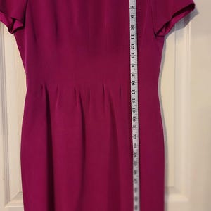 Peut inclure: Une robe magenta &agrave; manches courtes avec un col rond et une silhouette ajust&eacute;e. La robe est mesur&eacute;e avec un ruban &agrave; mesurer, montrant une longueur de 91,44 cm.