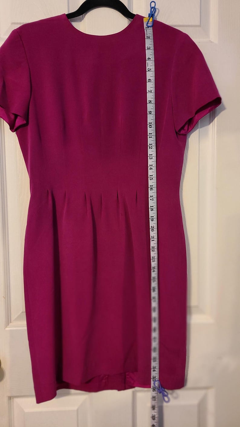 Peut inclure: Une robe magenta &agrave; manches courtes avec un col rond et une silhouette ajust&eacute;e. La robe est mesur&eacute;e avec un ruban &agrave; mesurer, montrant une longueur de 91,44 cm.