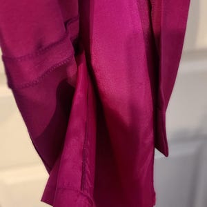 Peut inclure: Gros plan sur un tissu magenta avec une couture le long du bord. Le tissu est pli&eacute; et la couture est visible.