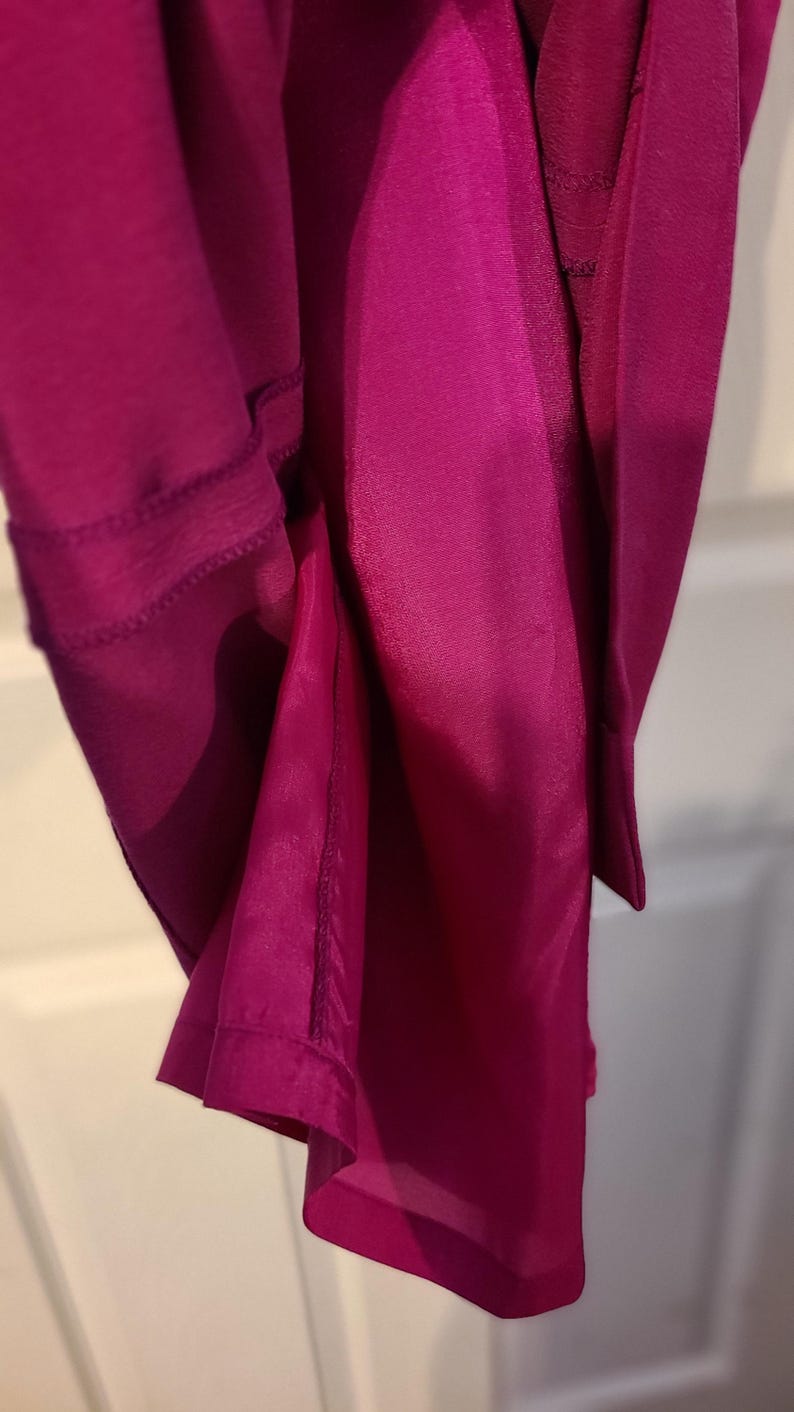 Peut inclure: Gros plan sur un tissu magenta avec une couture le long du bord. Le tissu est pli&eacute; et la couture est visible.