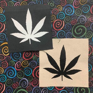 Puede incluir: Dos parches de tela con un diseño de hoja de marihuana. Un parche es negro con una hoja blanca, y el otro es blanco con una hoja negra.