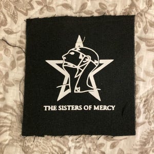 May include: A white ceramic mug with a black handle and the text "But First, Coffee" in a black, bold font. The mug is sitting on a wooden surface. The mug is approximately 4 inches tall.