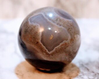 May include: A polished agate sphere with a swirling pattern of brown, grey, and white. The sphere is smooth and has a high gloss finish.