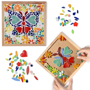 May include: Two mosaic art pieces in wooden frames. One shows a butterfly design, the other a butterfly in progress. Scattered around are loose mosaic tiles in various shapes and colours. The butterfly design includes red, blue, green, and orange tiles.