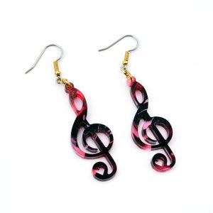 May include: A pair of pink and black treble clef earrings. The earrings are made of acrylic and have a swirl pattern.