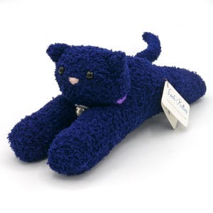 May include: A plush navy blue cat toy with a bell collar and a tag that reads "Sock Kitties." The cat has black button eyes, a pink nose, and a purple collar. The cat is lying down with its paws outstretched.