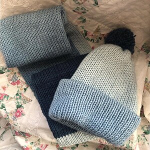 May include: A blue and white knitted hat with a pom pom on top and a matching blue and white knitted scarf.