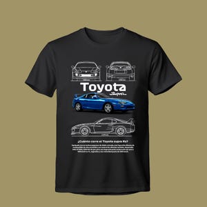 May include: A black t-shirt featuring a graphic print of a blue Toyota Supra car. The design includes white line-art diagrams of the car from the front, rear, and side, along with the text Toyota Supra and technical specifications in Spanish.