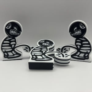 以下が含まれることがあります： 怒った顔と頭に8ボールが付いた、白黒の漫画のキャラクターが3体。キャラクターはスケルトンのようなデザインです。1体は横たわっており、他の2体は立っています。