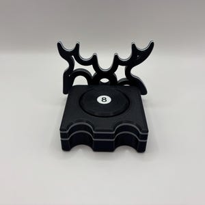 Puede incluir: Un porta bolas de billar negro con una bola blanca número ocho en el centro. El porta bolas está diseñado para contener varias bolas.