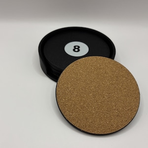 May include: A set of black circular coasters with a cork base. One coaster is separate, showing a brown cork surface. The top coaster has a white number 8 on a black background. The coasters are round and appear to be made of a durable material.