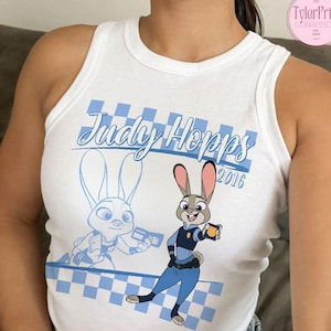May include: White vest top with a cartoon image of Judy Hopps from Zootropolis. The design includes the text "Judy Hopps 2016" in blue script, along with a checkered pattern and a cartoon image of Judy Hopps.