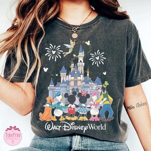 Puede incluir: Camiseta gris oscuro con un gr&aacute;fico colorido de personajes de Disney, un castillo, fuegos artificiales y Campanilla. El texto "Walt Disney World" est&aacute; impreso debajo. La camiseta tiene un aspecto vintage y desgastado.
