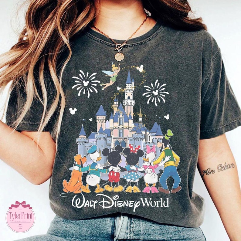 Puede incluir: Camiseta gris oscuro con un gr&aacute;fico colorido de personajes de Disney, un castillo, fuegos artificiales y Campanilla. El texto "Walt Disney World" est&aacute; impreso debajo. La camiseta tiene un aspecto vintage y desgastado.