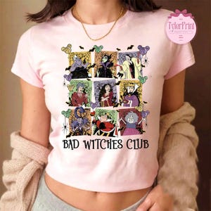 May include: A light pink t-shirt featuring a grid of cartoon villain illustrations. The shirt has the words "BAD WITCHES CLUB" printed in a bold font. The design includes bats, spiders, and Mickey Mouse-shaped balloons.