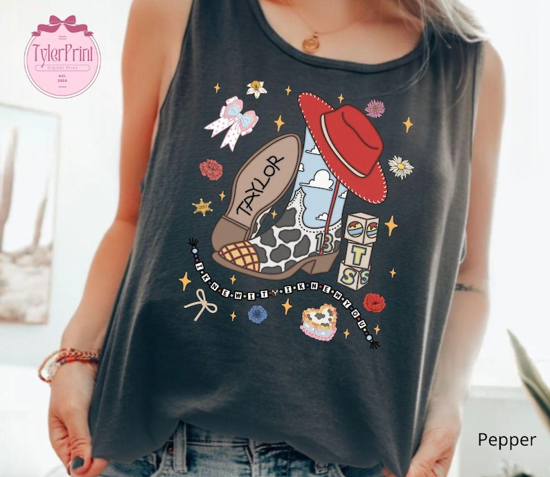 May include: A dark gray sleeveless tank top featuring a graphic print of a cow-print cowboy boot, a red hat, a beaded bracelet with the text "I KNEW YOU WERE", and blocks spelling "BTS". The boot includes the name "TAYLOR" and the number "13".
