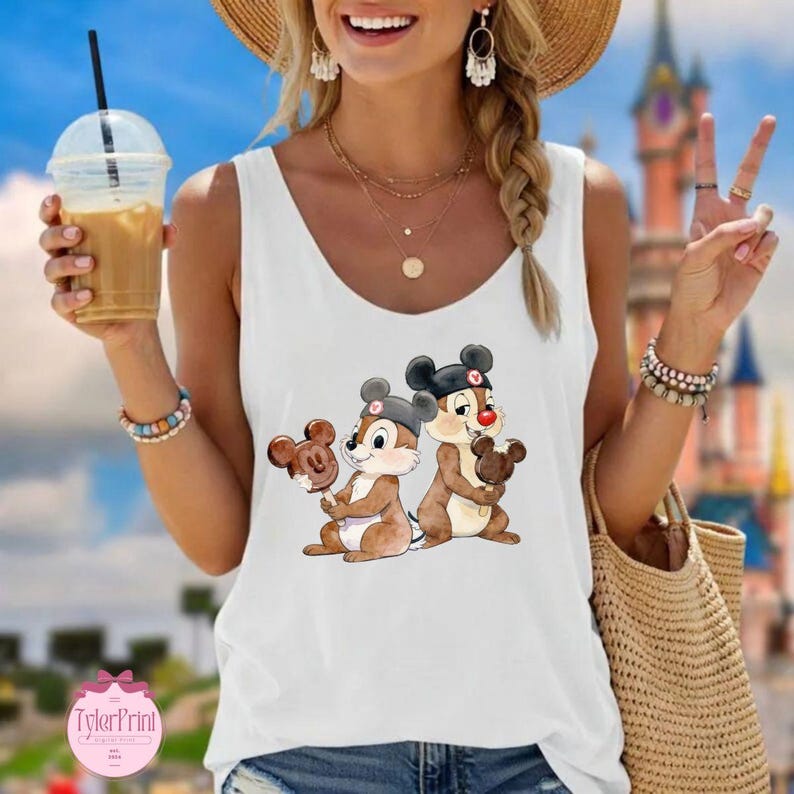 Puede incluir: Camiseta sin mangas blanca con un gr&aacute;fico de dibujos animados de Chip y Chop sosteniendo helados de Mickey Mouse. La imagen muestra a los personajes en marr&oacute;n y beige con sombreros negros y narices rojas. La camiseta sin mangas es sin mangas y tiene cuello redondo.