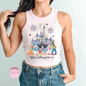 Puede incluir: Una camiseta sin mangas rosa claro con un gr&aacute;fico colorido del castillo de Walt Disney World, fuegos artificiales y personajes de Disney. El texto "Walt Disney World" est&aacute; impreso debajo. La camiseta sin mangas tiene una textura acanalada.