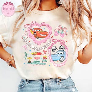 Puede incluir: Una camiseta blanca con un dise&ntilde;o gr&aacute;fico rosa y azul con coches de dibujos animados de la pel&iacute;cula Cars de Disney Pixar. El dise&ntilde;o incluye el texto "Best Day Ever" en un coraz&oacute;n rosa.