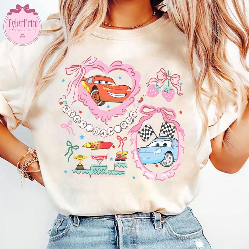Puede incluir: Una camiseta blanca con un dise&ntilde;o gr&aacute;fico rosa y azul con coches de dibujos animados de la pel&iacute;cula Cars de Disney Pixar. El dise&ntilde;o incluye el texto "Best Day Ever" en un coraz&oacute;n rosa.