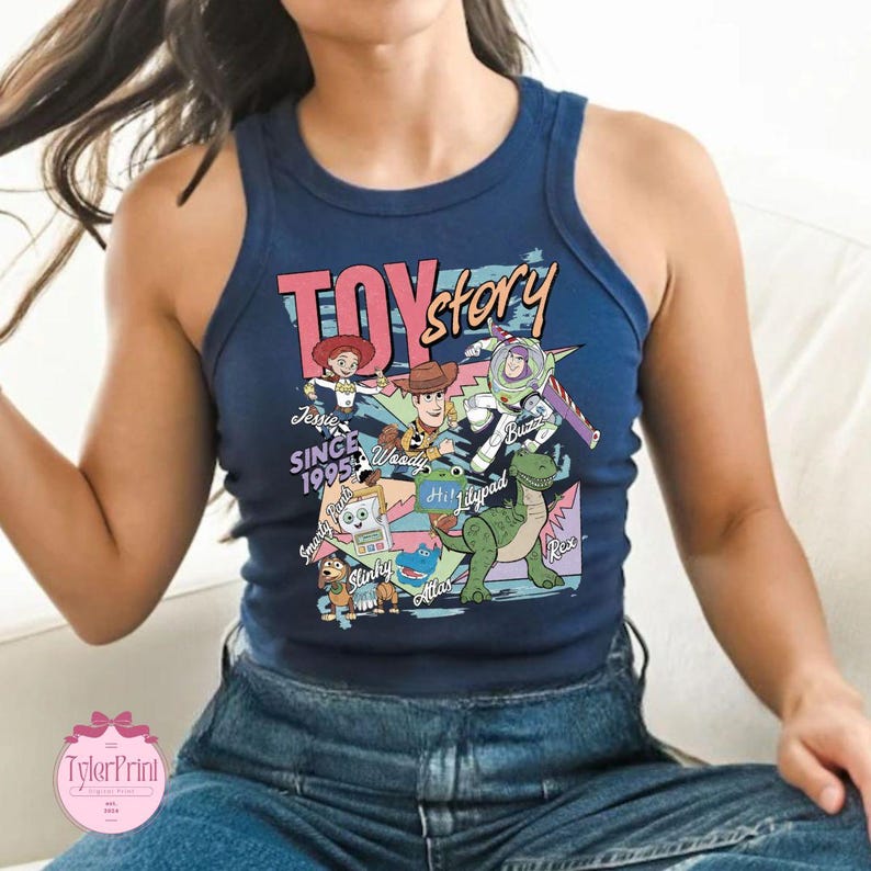 K&ouml;nnte beinhalten: Ein dunkelblaues &auml;rmelloses Tanktop mit einem Grafikdruck von Toy Story-Figuren, darunter Woody, Buzz Lightyear, Jessie, Rex und Slinky. Das Design enth&auml;lt den Text Toy Story, Since 1995 sowie die Namen der Figuren in verschiedenen Schriftarten.