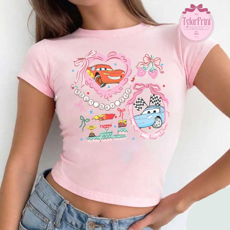 Puede incluir: Camiseta rosa de manga corta y corte corto con un gr&aacute;fico de dibujos animados de Rayo McQueen y Mate de la pel&iacute;cula Cars. El gr&aacute;fico incluye el texto "Best Day Ever" con corazones, estrellas y lazos.