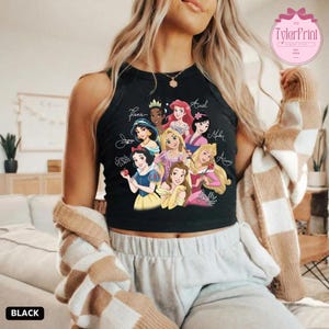 May include: Black tank top featuring a colorful graphic of Disney princesses, including Snow White, Ariel, and Belle. The princesses' names are written above them in a cursive font. The word "BLACK" is printed at the bottom.