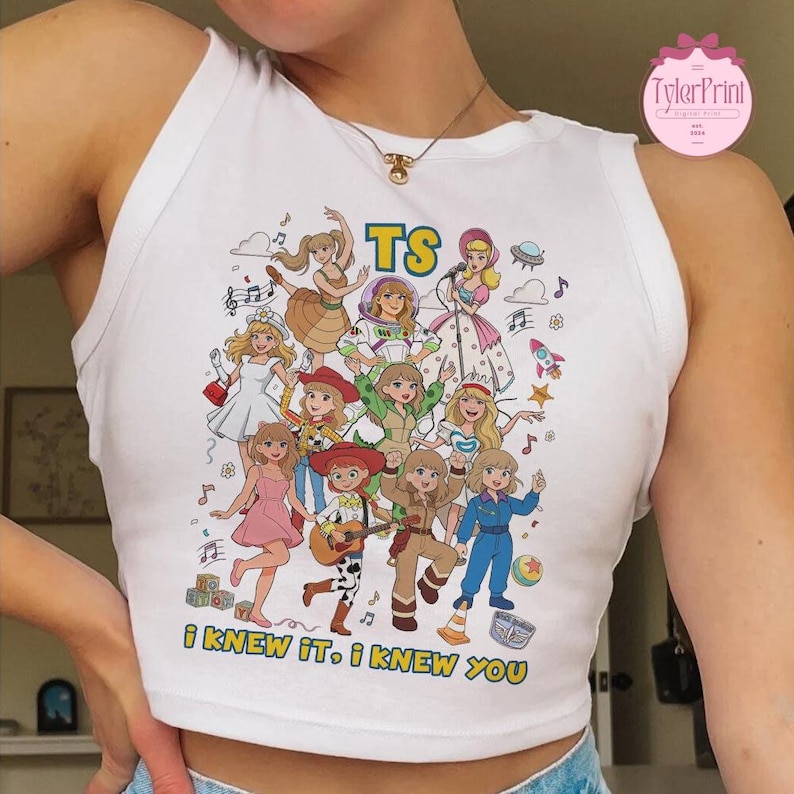 May include: A white sleeveless tank top featuring a colorful graphic print of multiple cartoon characters in various outfits. The text TS is printed at the top, and the phrase I KNEW IT, I KNEW YOU is printed at the bottom in yellow lettering.