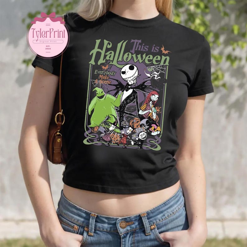 K&ouml;nnte beinhalten: Schwarzes T-Shirt mit einem Halloween-Motiv mit Jack Skellington, Sally und Oogie Boogie. Der Text auf dem Shirt lautet "This is Halloween" und "Everybody Make a Scene". Das Design beinhaltet Flederm&auml;use und ein Spinnennetz.