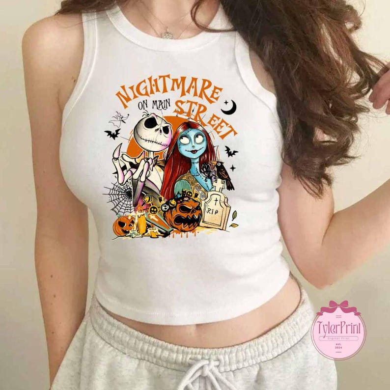 K&ouml;nnte beinhalten: Wei&szlig;es Tanktop mit einem farbenfrohen Aufdruck von Jack Skellington und Sally aus The Nightmare Before Christmas. Das Design umfasst K&uuml;rbisse, Flederm&auml;use und den Text "Nightmare on Main Street."
