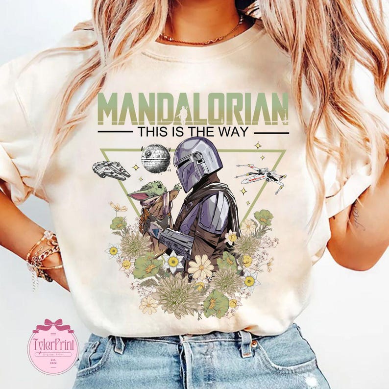 May include: Cream-colored t-shirt featuring a graphic of The Mandalorian and Grogu surrounded by flowers. The text "MANDALORIAN - THIS IS THE WAY" is printed above the characters. Includes images of a spaceship and the Death Star.