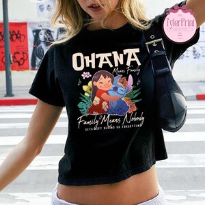 May include: Black t-shirt featuring the words "OHANA Means Family" and "Family Means Nobody Gets Left Behind or Forgotten." The shirt has a graphic of a girl hugging a blue alien character, surrounded by flowers.