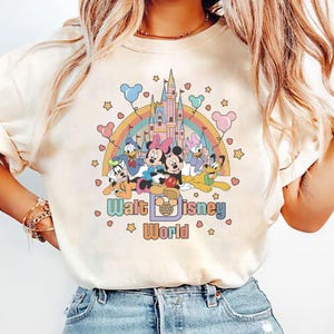 May include: A white t-shirt with a colorful graphic of Mickey Mouse and friends in front of the Disney castle. The graphic also includes a rainbow and stars. The text "Walt Disney World" is printed below the graphic.